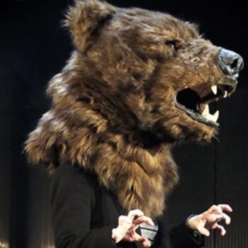 A person in a bear head mask with hands in claw shapes